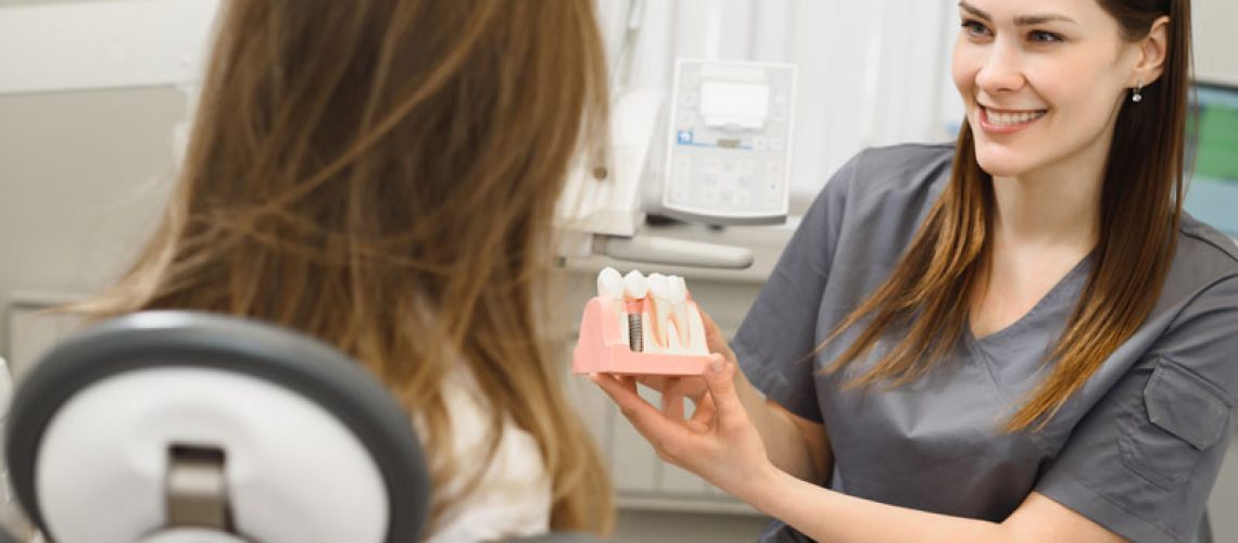 a dental assistant showing a patient a dental implant model